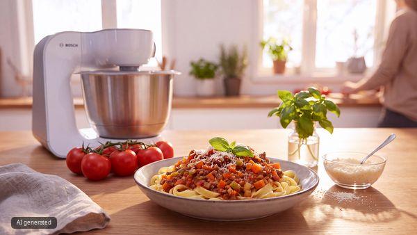 Ein Teller mit verzehrfertiger Bolognese steht auf einer K&uuml;chenarbeitsplatte. Dahinter steht eine K&uuml;chenmaschine von Bosch.