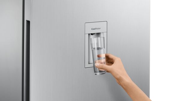 Persons hand holding glass against Bosch Fridge Freezer water dispenser