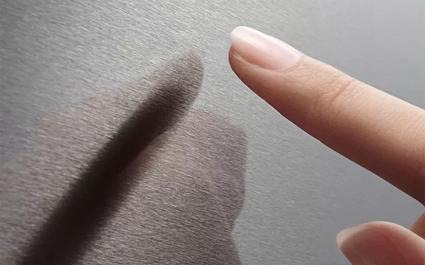 Plan rapproché d'un doigt qui touche une belle surface en acier inoxydable, mettant en valeur sa texture lisse et son éclat.