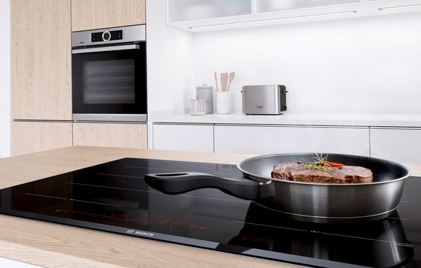 The vapour from a frying pan is extracted into a hood above the cooktop.