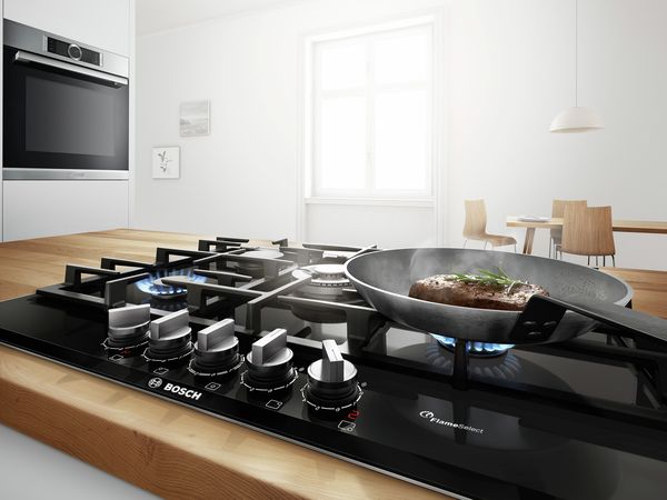 Bosch gaskookplaat met pan in keukeneiland met inbouwoven op de achtergrond