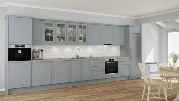 Large grey single-wall farmhouse kitchen with built-in Bosch ovens. One in the top cabinet and one below the stone worktop. MUM food processor on counter. Kitchen table and sitting nook on the right. 