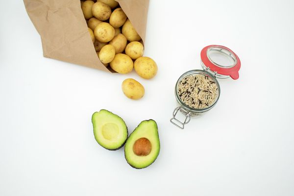 A fully packed paper bag containing potatoes with a half-cut avocado and portion of wild rice as ingredients for delicious avocado side dishes.