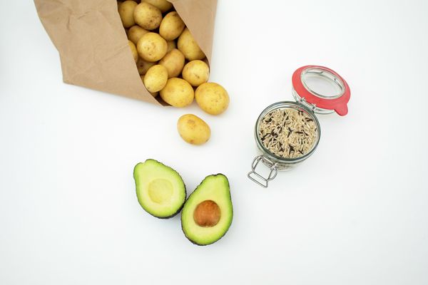 Un sacchetto di carta stracolmo di patate, con un avocado tagliato a metà e una porzione di riso selvatico come ingredienti per deliziosi contorni a base di avocado.