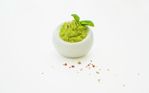 Eine Avocadohälfte neben Pfeffer, Knoblauch und einer fertigen Guacamole mit einem Stück Limette.