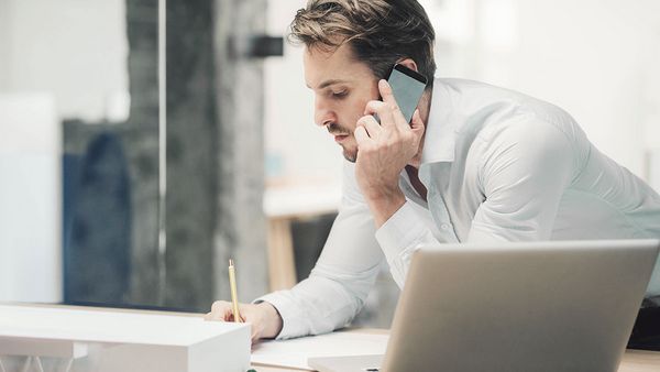 Homme au t&eacute;l&eacute;phone prenant des notes avec un ordinateur portable ouvert