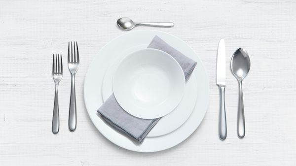 Детайли от подредена маса за вечеря с добре аранжирани чинии, чаша с вода и малка купа с хапки.