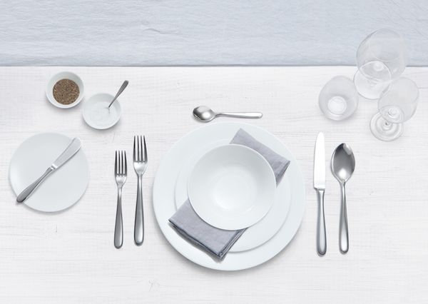 Detalji stola spremnog za večeru s klasičnim bijelim tanjurima, priborom i prstenom za ubruse.