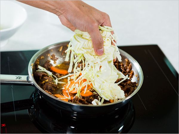 Adding the sliced carrots and cabbage to the beef