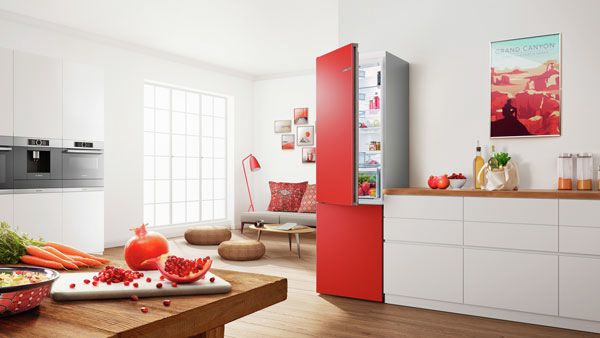 Roter, freistehender Kühlschrank von Bosch in einem modernen Raum, daneben ein Sofa und ein Kaffeetisch.