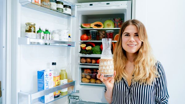 Woman holding large jar of drink next to open fridge