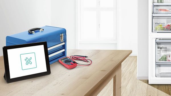 Ipad with repair service next to toolkit on a kitchen top with fridge in the background.