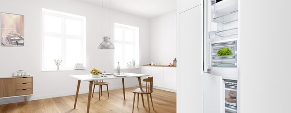 Indbygget Bosch køle-/fryseskab med dørene lidt på klem, i hvidt køkkenskab ved siden af moderne spisestue.