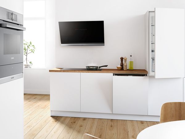 Black Bosch oven, hood fan and hob, plus built-in dishwasher and fridge, in modern white kitchen.