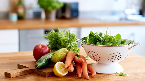 Frisches Gemüse liegt in einer Schüssel und auf einem Holzbrett in einer Küche.