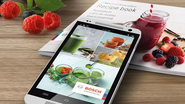 Angled shot of recipe book and phone with web app on screen on a kitchen table.