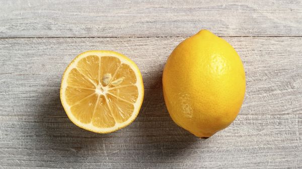 Limone intero e limone tagliato a met&agrave; appoggiati su un piano in legno chiaro