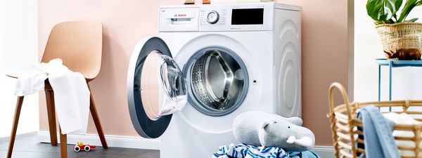 Close up of a white washing machine with laundry basket and toys lying around