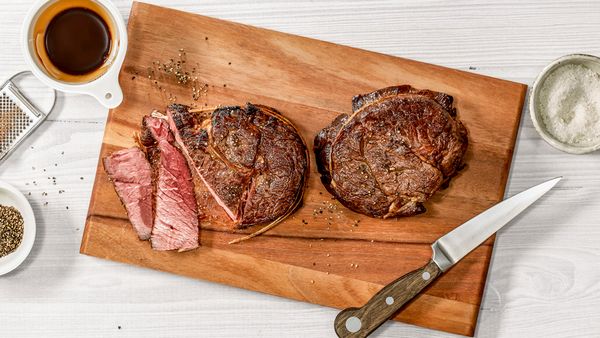 Zwei Steaks mit Röstaromen liegen neben einem Messer auf einem Holzbrett.