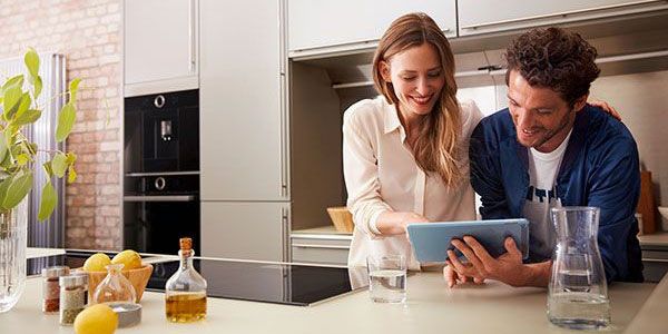 Un jeune couple lit les actualités Cookit sur une tablette dans sa cuisine moderne.