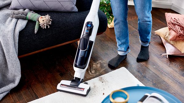 Woman vacuum cleaning next to a sofa