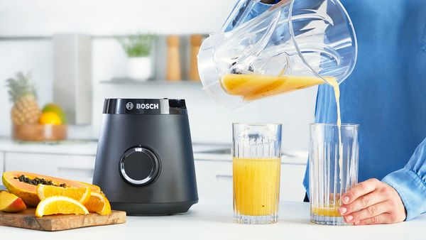 Person adding ice cubes to a Bosch blender to make a green smoothie.