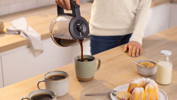 Eine Person gießt Kaffee aus der Glaskanne einer Filterkaffeemaschine in eine Tasse.